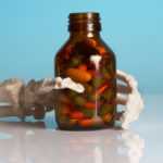 Skeleton hand holding a brown bottle full of pills